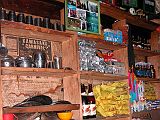 Manaslu 06 11 Syala Lodge Shop The hotel also doubles as a general store. On the left shelves are household cups and bowls,  beer, and paint. In the middle shelves are clothes detergent, cookies, batteries, more beer, butter, Chinese wine, and another can of paint. On the right hand shelves are nail polish, two rows of whisky, noodles, butter, Chinese dish powder, and Goldstar sneakers. Family photos hung proudly near the top.